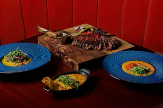 Delicious grilled steak with bone marrow on a wooden board, surrounded by blue plates and flavorful skillet dishes.