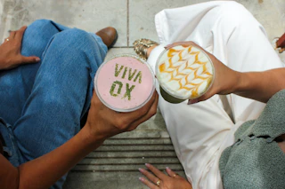 Two people enjoy vibrant drinks—one bright pink with “VIVA OX” in green, the other topped with beautiful caramel art.