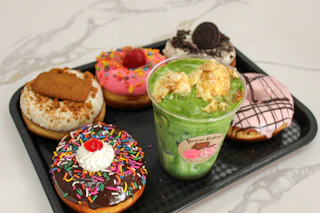 A tray of vibrant donuts and a refreshing green dessert drink with crunchy toppings, perfect for a delightful treat.