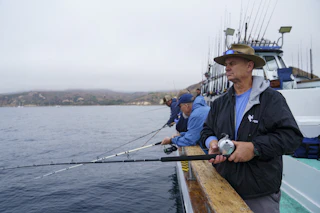 Guests enjoy a scenic fishing trip from a boat, rods ready, dressed warmly for a pleasant day on the water.