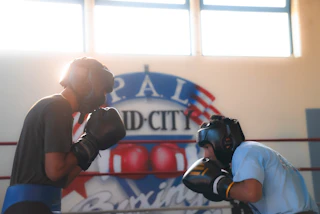 Sunlit gym with two boxers sparring in a friendly match, vibrant atmosphere and gym logo in the background.