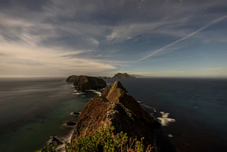 Rocky islands stretch into the ocean beneath a sparkling starry sky, with gentle clouds and peaceful waters embracing the coast.