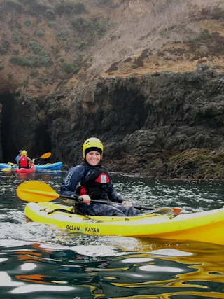 Smiling kayaker enjoys a scenic adventure on the water, with fellow paddlers exploring stunning rocky cliffs in the background.