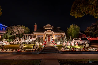 A charming house aglow with colorful Christmas lights and cheerful reindeer displays creates a festive nighttime scene.