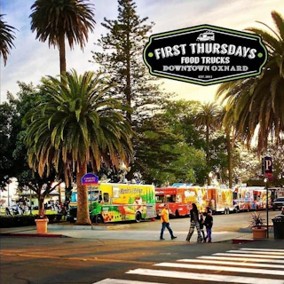Vibrant food trucks under palm trees at sunset welcome visitors to First Thursdays in downtown Oxnard, with people enjoying the scene.