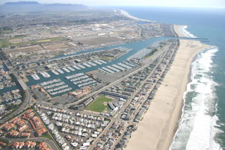 Stunning aerial view of a vibrant coastal city featuring a picturesque marina, golden sandy beach, sparkling ocean waves, and charming neighborhoods.