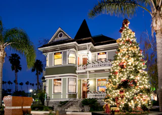 Charming Victorian house with a beautifully decorated, glowing Christmas tree welcoming visitors at dusk.