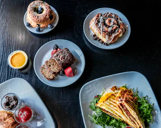 An inviting table features delicious pastries, brownies, fresh fruit, and savory crepes with greens and sauces on elegant white plates.