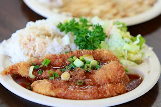 Delicious breaded fish fillets with savory sauce, fluffy steamed rice, and fresh salad, beautifully garnished with herbs.