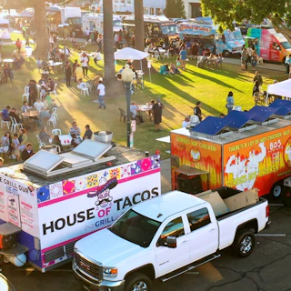 A vibrant outdoor food truck festival in a green park, with visitors enjoying delicious meals at tables beside colorful trucks.