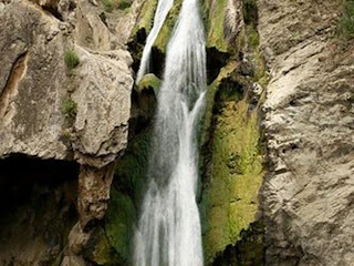 A stunning waterfall cascades over lush mossy rocks into a tranquil pool, framed by dramatic, scenic rocky cliffs.