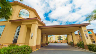 Grand tan hotel entrance with impressive columns and elegant arched windows, set beneath a beautiful partly cloudy blue sky.