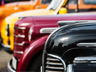 Vibrant vintage cars—black, red, yellow, and orange—parked in a cheerful row, showcasing classic charm for visitors to enjoy.
