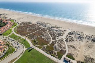 Stunning aerial view of a golden sandy beach, sparkling ocean waves, scenic paths, and a lush green park with swaying palm trees.