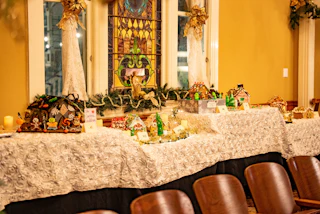 A charming display of gingerbread houses on a festively decorated table set before a colorful stained glass window and holiday garland.