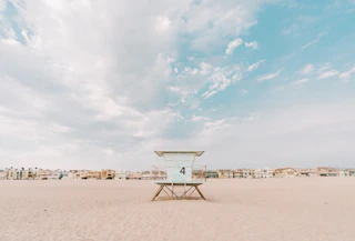Lifeguard tower 4 stands on a beautiful sandy beach, with charming houses and a bright sky filled with picturesque clouds.