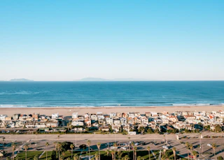 Aerial view of a charming coastal town featuring inviting houses, a golden sandy beach, and gentle ocean waves under sunny skies.