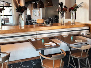 Bright, inviting restaurant with stylish wooden tables, cozy striped seating, chic chairs, and cheerful flowers on a partition.