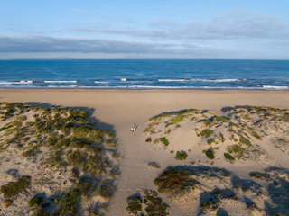 A scenic sandy path winds through picturesque dunes to a beautiful, tranquil beach with soft waves beneath a lovely sky.