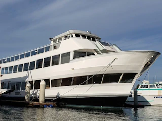 A beautiful white yacht docked at a vibrant marina, with another boat in the background beneath a clear, sunny blue sky.