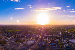 Stunning aerial view of a vibrant city at sunset, golden sun low in the sky, illuminating the skyline and lively streets below.