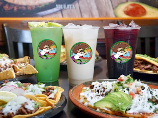 A vibrant table set with three colorful drinks and delicious Mexican dishes like tacos and nachos, perfect for a festive meal.