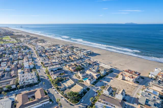 Stunning aerial view of a vibrant coastal town with charming beachfront homes, golden sands, and sparkling blue ocean under sunny skies.